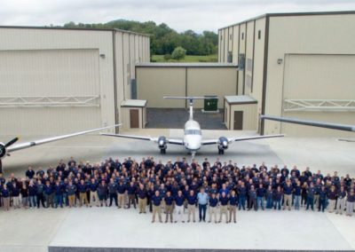 Drone photo of team in front of hangars with planes in background