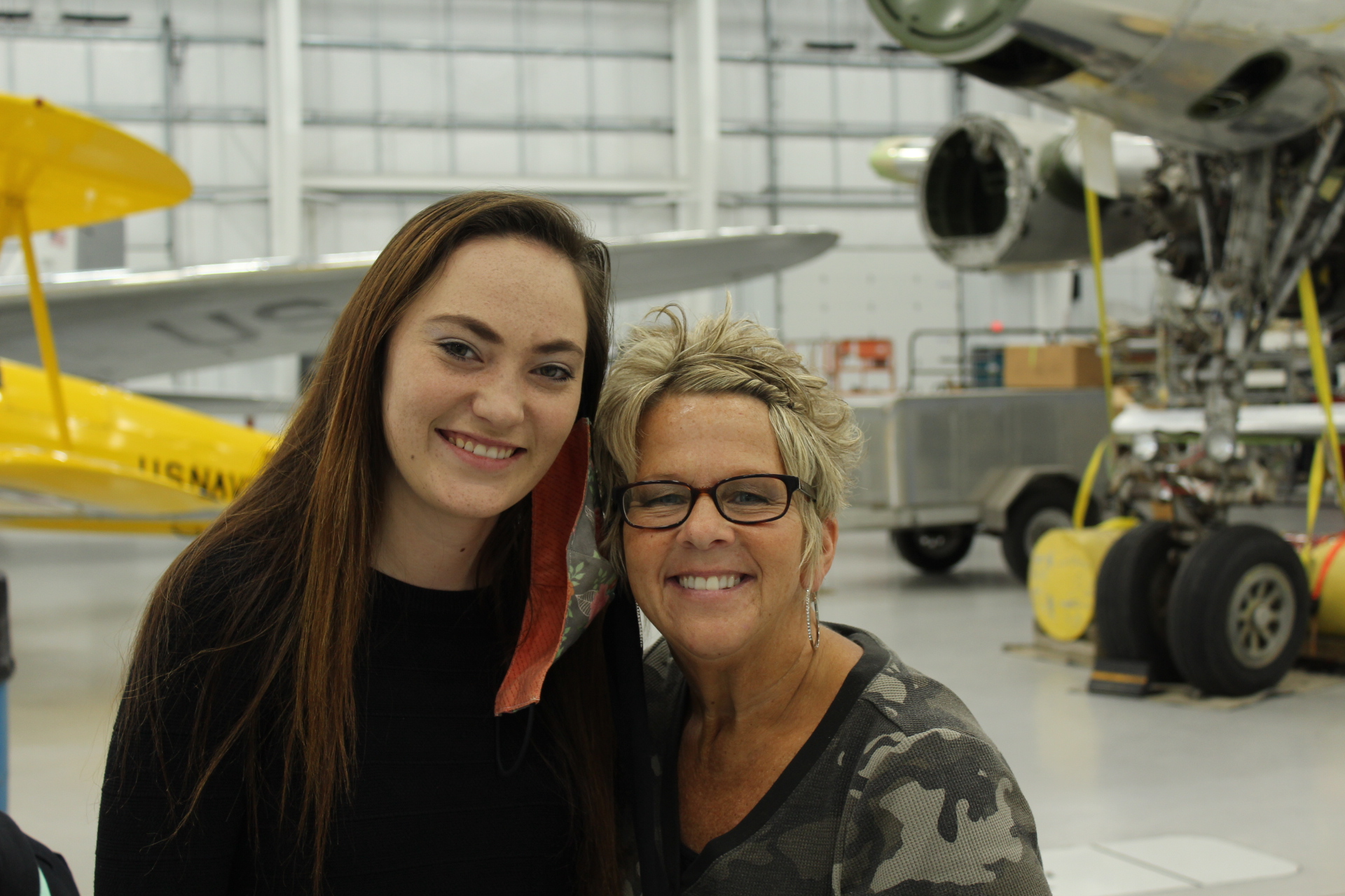 A mother and daughter smile for the camera in a hangar.